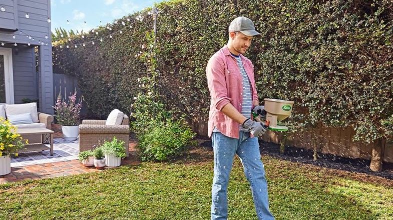 Homeowner applying a lawn treatment with a handheld spreader